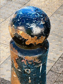 Photograph: Old blue pavement bollard with lots of rust patches.